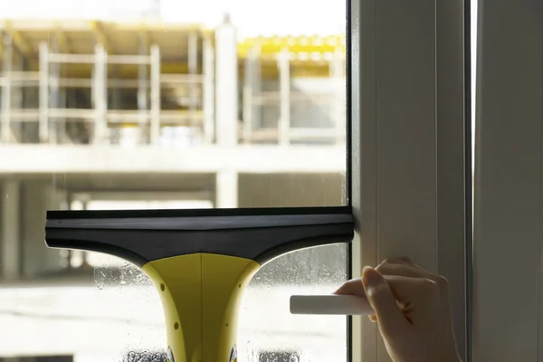 Wash the window at home with a battery wiper. The apparatus yellow collects drops of water and clean the window. Hands scrub the window. White window frame with a handle.