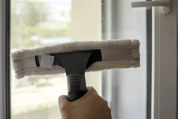 Wash the window at home with a battery wiper. The apparatus yellow collects drops of water and clean the window. Hands scrub the window. Hands wipe the glass with a soft scraper.