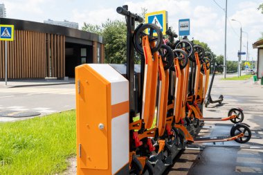 Yolun yakınındaki Scooter kiralama istasyonu. Savunmada turuncu scooterlar. Şehirdeki mobiletlerin kirası ödenmiş. Yağmurdan sonra güneşli bir gün. Modern şehir taşımacılığı.