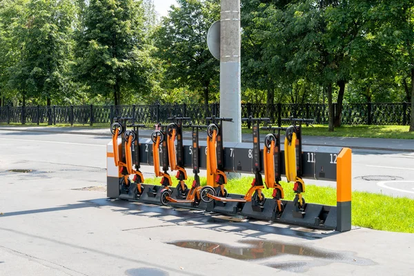 Scooter rental station near the road. Orange scooters in defense. Paid rental of scooters in the city. Sunny day after the rain. Modern city transport.