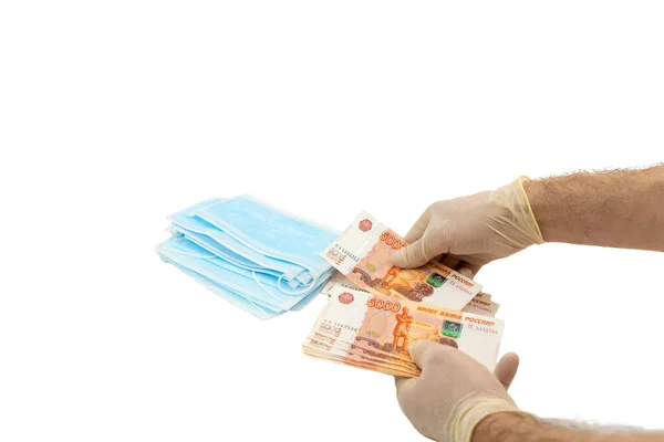 Beyaz koruyucu eldivenli iki el 5000 rublelik banknotlarla bir paket mavi tıbbi maske satın alır. Rusya 'dan maske alma fikri, virüse karşı koruma. Tıbbi maske kıtlığı, yüksek maliyetli. İzole edilmiş beyaz arkaplan.