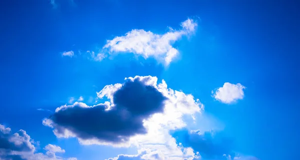 The bright sun breaks through the white cloud, the rays of the sun break through. Blue bright clear sky. Designer background.