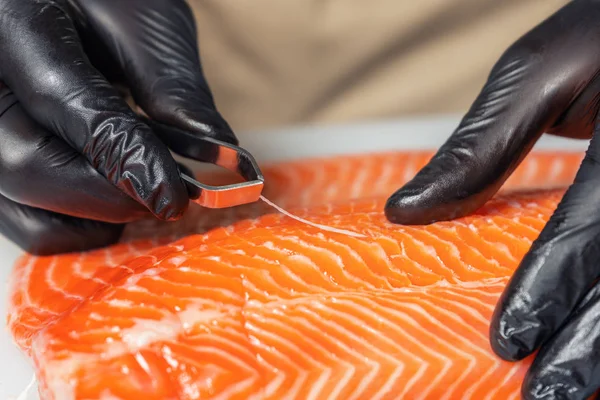 Chef\'s hands with tweezers remove the bones from the salmon fill