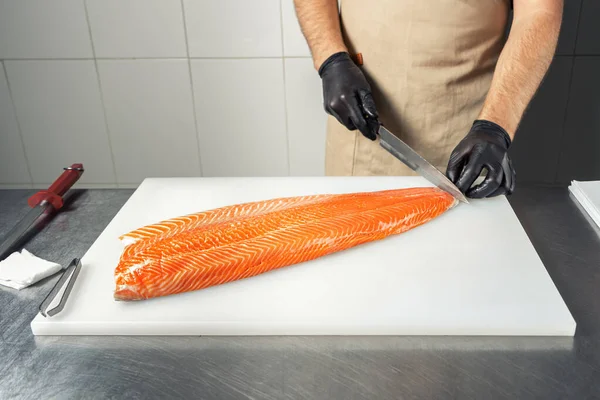 The chef cuts the skin off a salmon fillet on a white chopping Board.