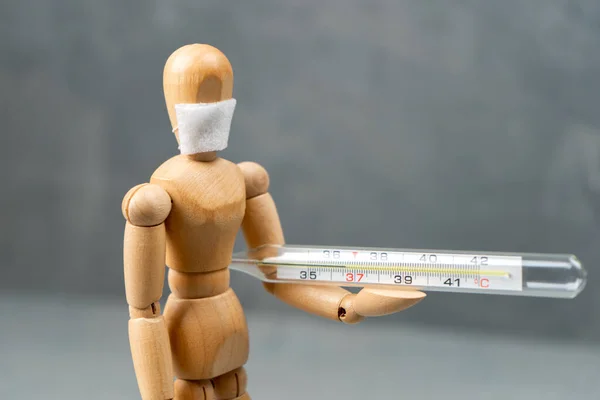 Wooden mannequin in a medical mask with a thermometer in his hands