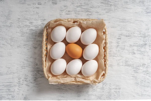 One orange egg among the white eggs in one wicker basket. Top view.