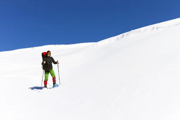 Senderismo de invierno en las montañas en raquetas de nieve con una mochila y tienda de campaña . — Foto de Stock