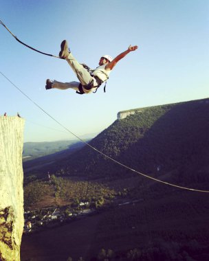 Rope jumping.Jump off a cliff into a canyon with a rope. clipart