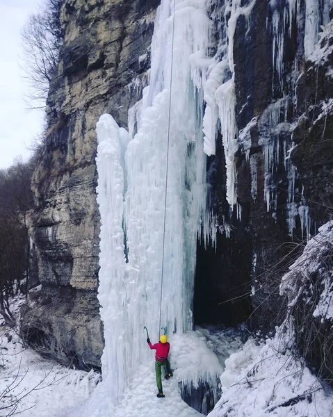 Ice climbing.Man climbing a frozen waterfall with ice tool.