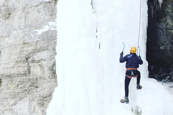 Arrampicata su ghiaccio.Uomo che scala una cascata ghiacciata con l'attrezzo del ghiaccio . — Foto Stock