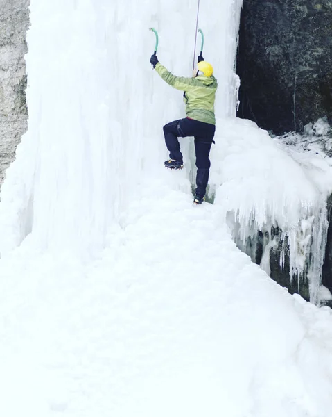 Arrampicata su ghiaccio.Uomo che scala una cascata ghiacciata con l'attrezzo del ghiaccio . — Foto Stock