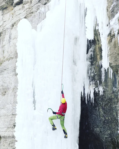 Arrampicata su ghiaccio.Uomo che scala una cascata ghiacciata con l'attrezzo del ghiaccio . — Foto Stock