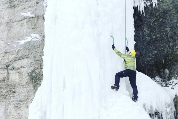 Arrampicata su ghiaccio.Uomo che scala una cascata ghiacciata con l'attrezzo del ghiaccio . — Foto Stock