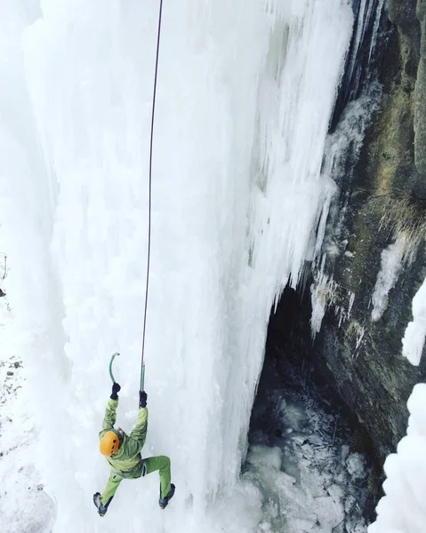 Arrampicata su ghiaccio.Uomo che scala una cascata ghiacciata con l'attrezzo del ghiaccio . — Foto Stock