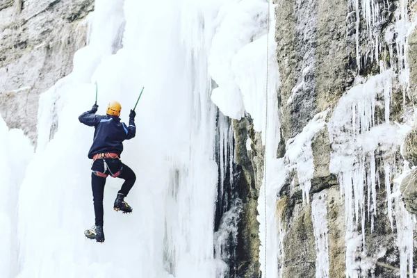 Ice climbing.Man climbing a frozen waterfall with ice tool.