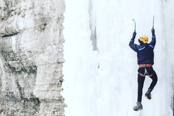 Arrampicata su ghiaccio.Uomo che scala una cascata ghiacciata con l'attrezzo del ghiaccio . — Foto Stock