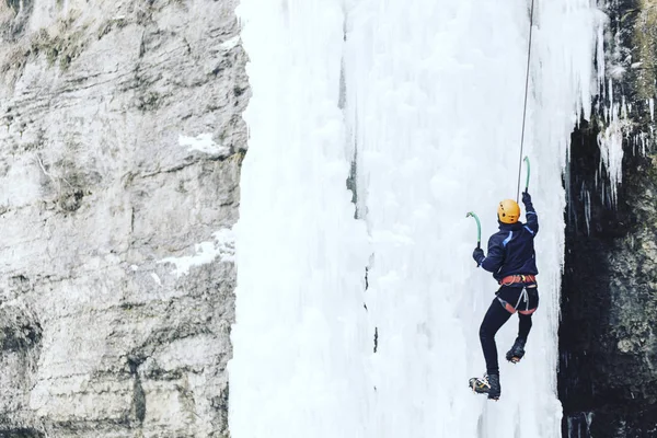 Isklättring. Man klättrar ett fruset vattenfall med is verktyg. — Stockfoto