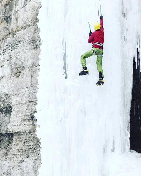 Arrampicata su ghiaccio.Uomo che scala una cascata ghiacciata con l'attrezzo del ghiaccio . — Foto Stock