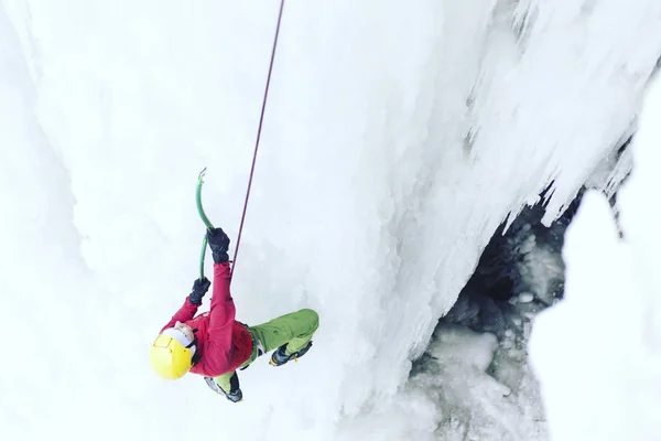 Arrampicata su ghiaccio.Uomo che scala una cascata ghiacciata con l'attrezzo del ghiaccio . — Foto Stock