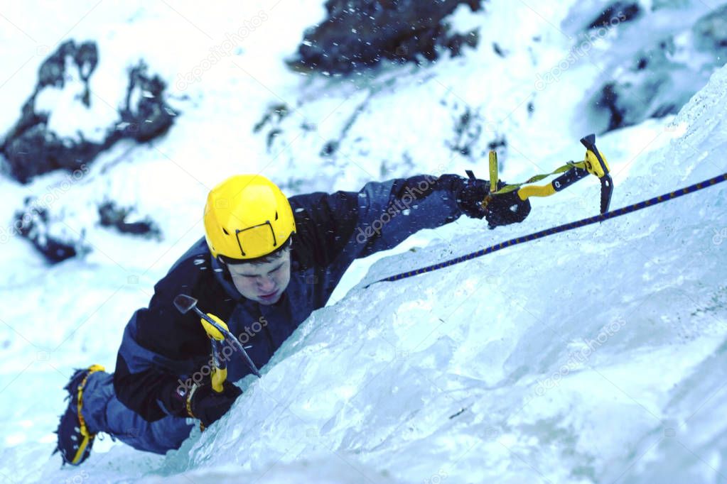 Ice climbing.Man climbing a frozen waterfall with ice tool.