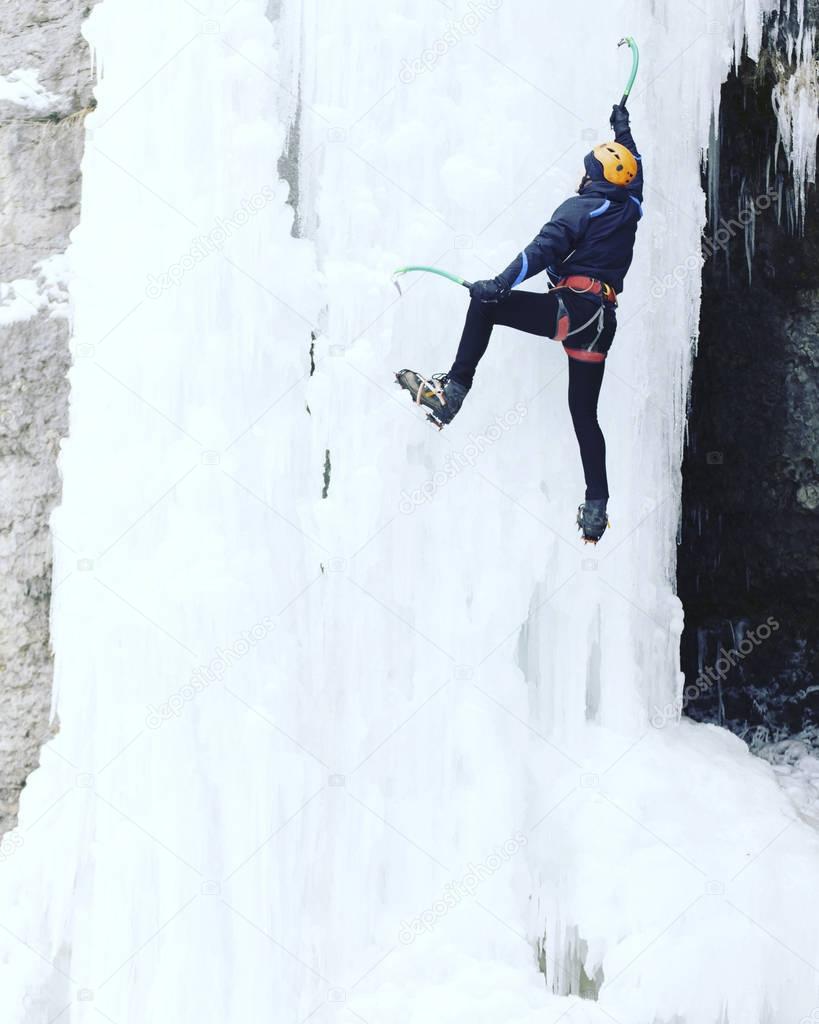 Ice climbing.Man climbing a frozen waterfall with ice tool.