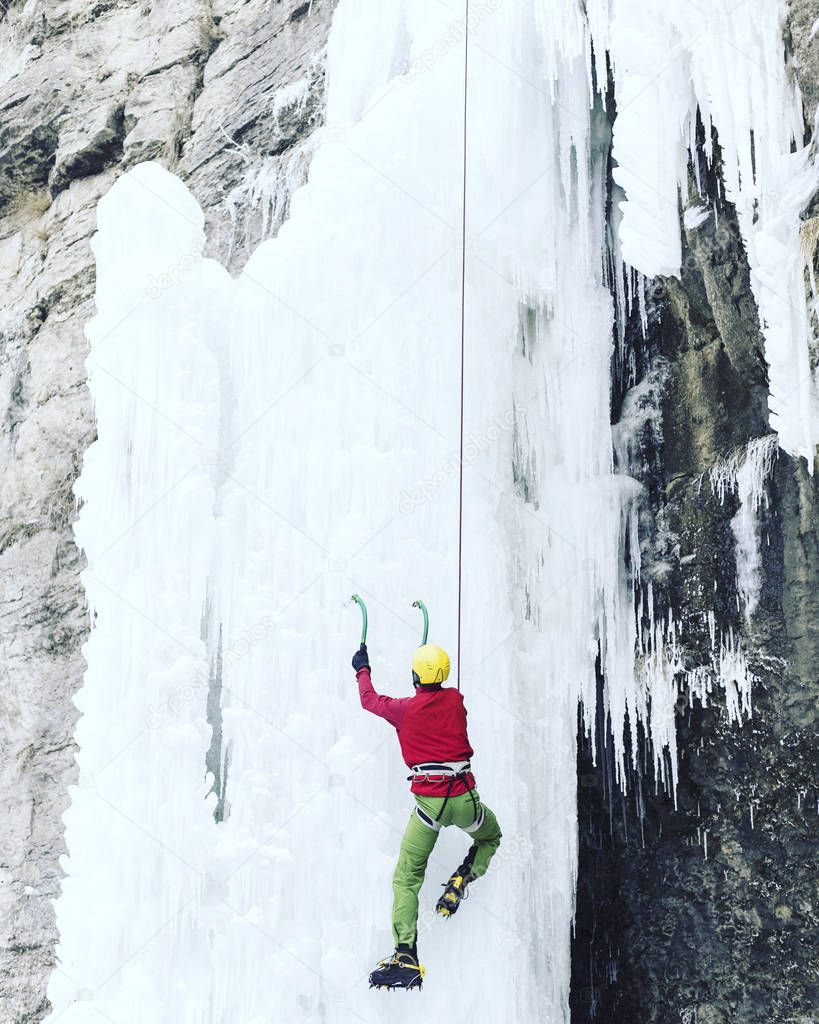 Ice climbing.Man climbing a frozen waterfall with ice tool.