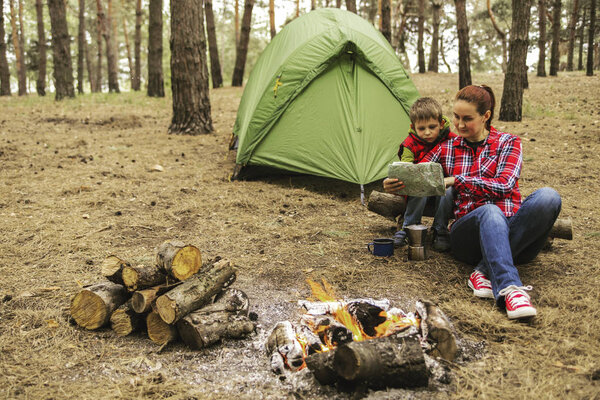 Camping in the forest. Mom and son are sitting near the fire pre