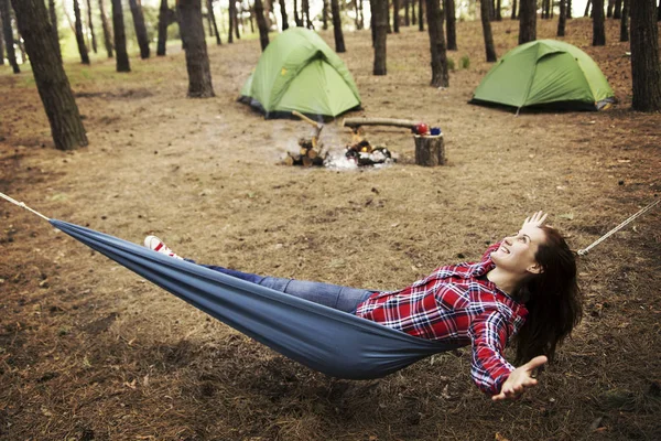 Camping in the forest. The girl sits in a hammock and looks at t — Stock Photo, Image