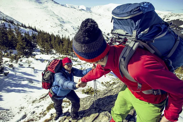 Climber helping teammate climb the man with the backpack reached