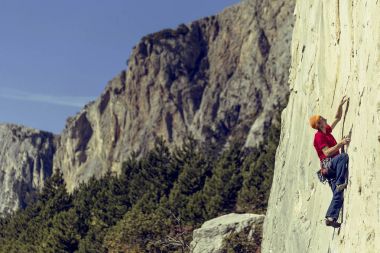 genç adam bir vadide Dağları ile kayalık bir duvara tırmanıyor..