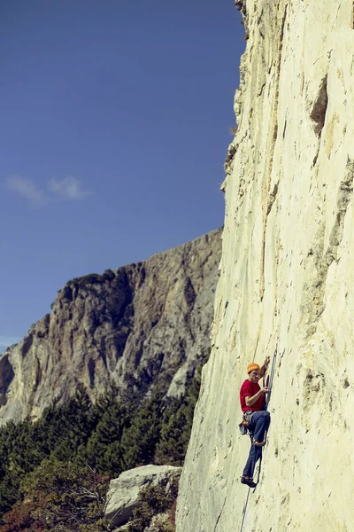 Jeune homme grimpe sur une paroi rocheuse dans une vallée avec des montagnes . — Photo