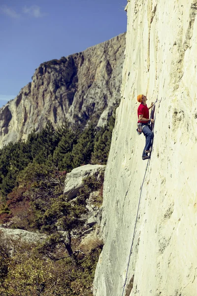 Молодой человек взбирается на скалистую стену в долине с горами . — стоковое фото
