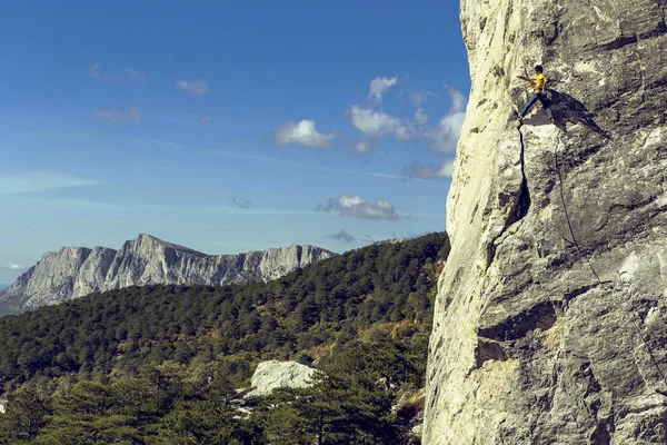 Young man climbs on a rocky wall in a valley with mountains. — Stock Photo, Image