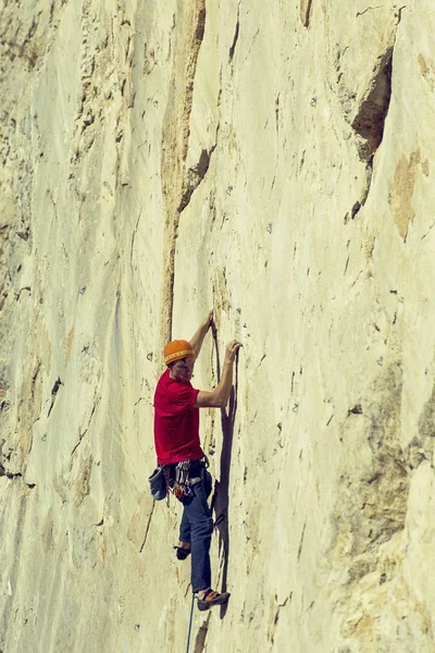 Young man climbs on a rocky wall in a valley with mountains. — Stock Photo, Image