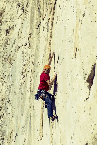 Молодой человек взбирается на скалистую стену в долине с горами . — стоковое фото