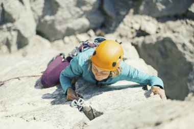 Bir kadın dağcı bir uçurumun tepesine tırmanıyor.