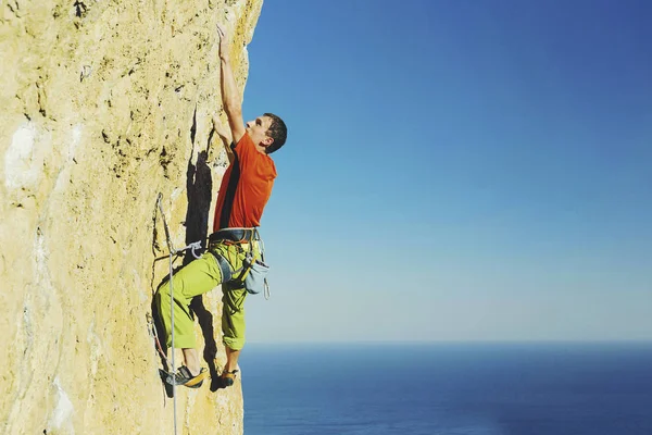 En man klättring på klippor mot bakgrund av havet. — Stockfoto