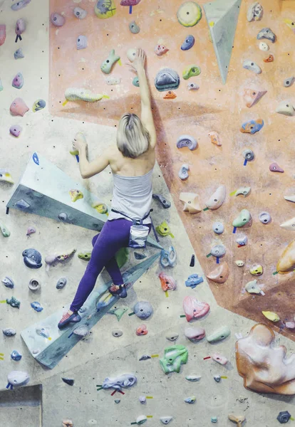 Mujer joven practicando escalada en roca en una pared de roca en el interior — Foto de Stock