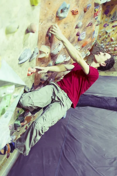 Young man practicing rock-climbing on a rock wall indoors. — Stock Photo, Image