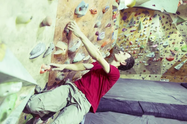 Joven practicando escalada en roca en una pared de roca en el interior . — Foto de Stock
