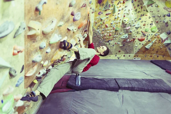 Joven practicando escalada en roca en una pared de roca en el interior . —  Fotos de Stock
