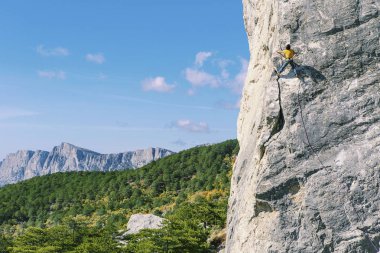 Adam dağcı. Kaya tırmanışçısı kayalık bir duvara tırmanıyor. Adam yapar