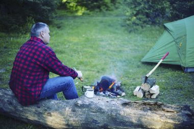 Bir adam kampta yangın kahvaltıda hazırlanıyor.