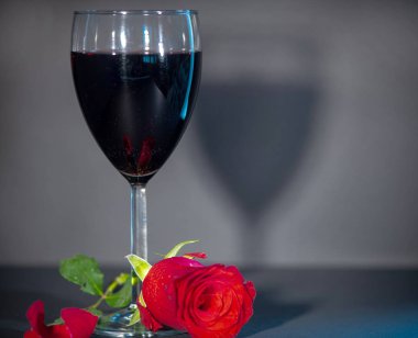 Koyu gri arka planda kırmızı şarap ve kırmızı gül.