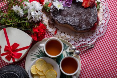 2 fincan çay, limon, zencefil, kek, karanfil ve kareli masa örtüsü üzerinde kalp şeklinde bir kutu.