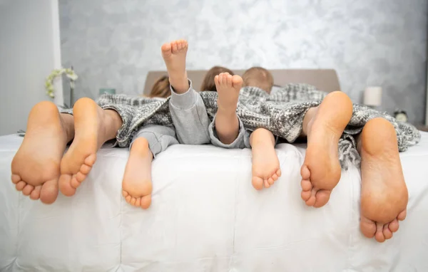 Evde kal, yatakta dört çift bacak ebeveynler ve çocuklar.