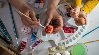 Çocuklar Paskalya yumurtalarını resim malzemeleriyle boyarlar. Anne ve bebek paskalya yumurtalarını boyar.. 