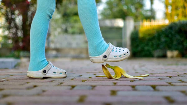 歩道を歩くバナナの皮とその上を歩く足は — ストック写真