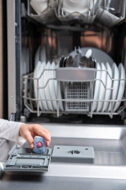 Çocuk eli bulaşık makinesine deterjan koyuyor.