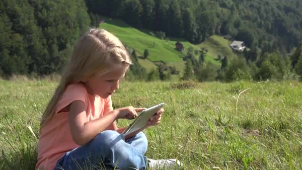 4K Kid spelen op Tablet, Kind speelt op weide, Meisje met behulp van werkende smartphone op een reis in de bergen — Stockvideo